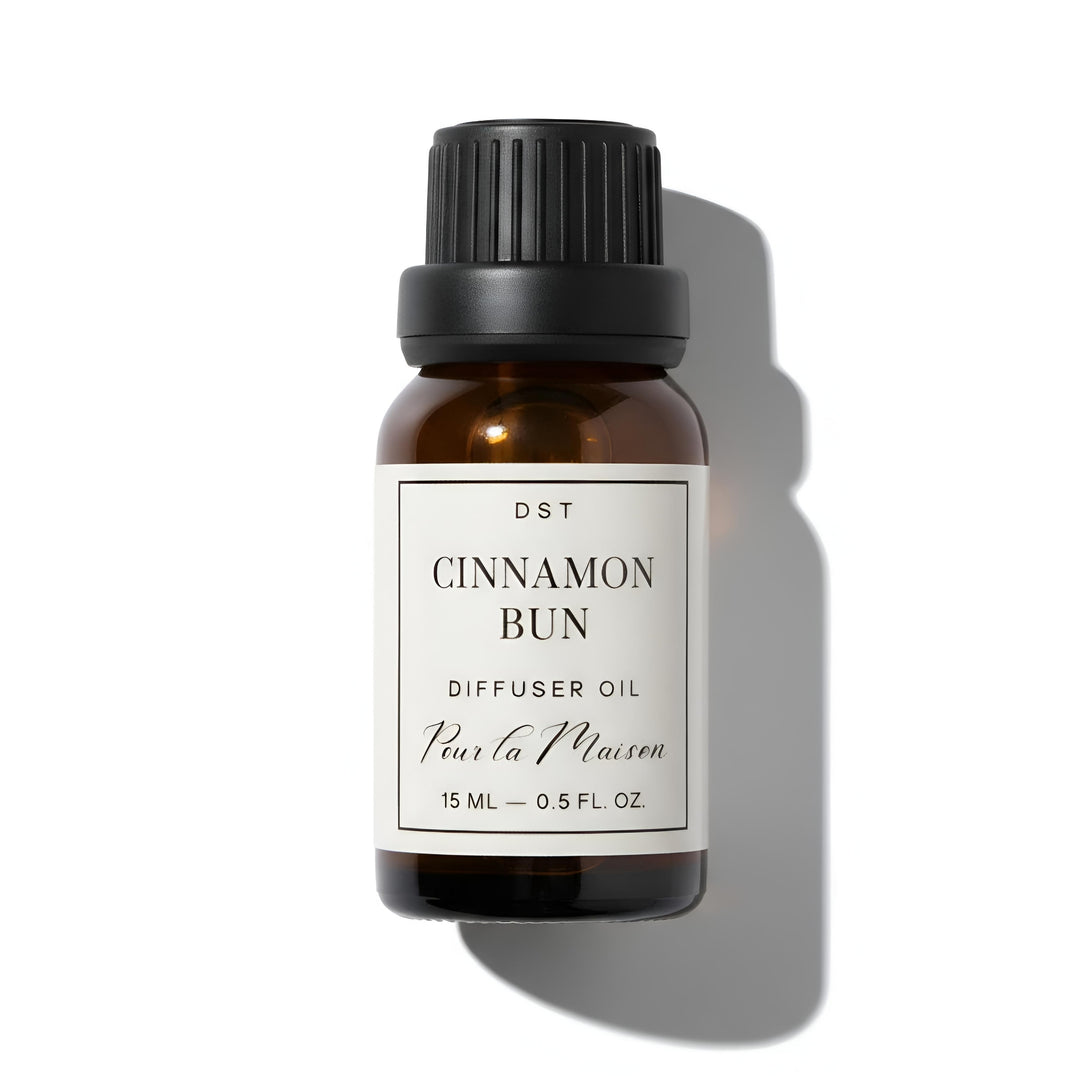 Bottle of Cinnamon Bun diffuser oil on a wooden coaster with cinnamon bun decorations in the background.