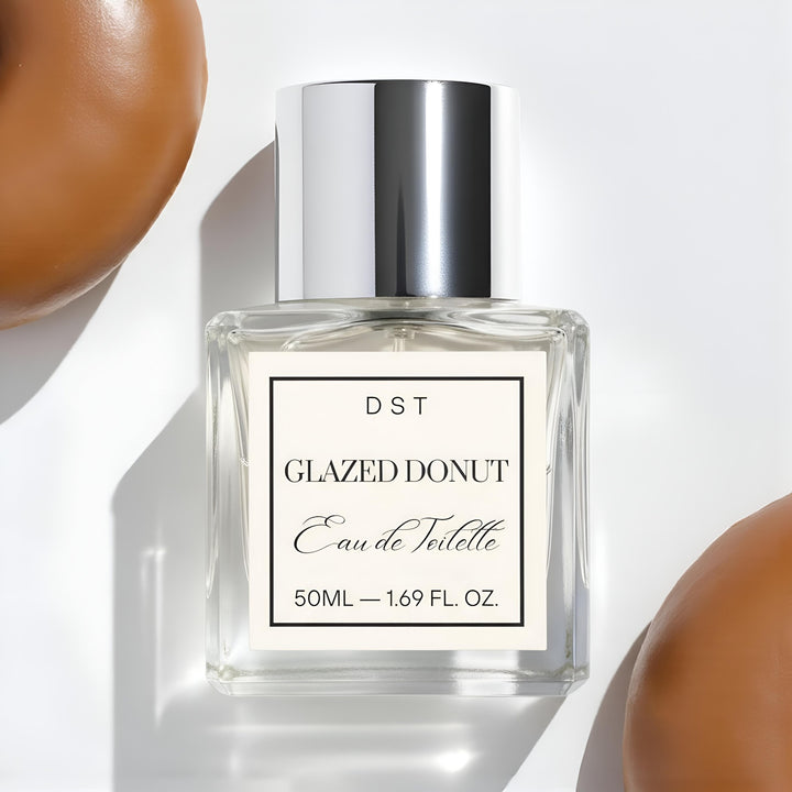 Perfume bottle labeled 'Glazed Donut' by DST with donuts around on a light background