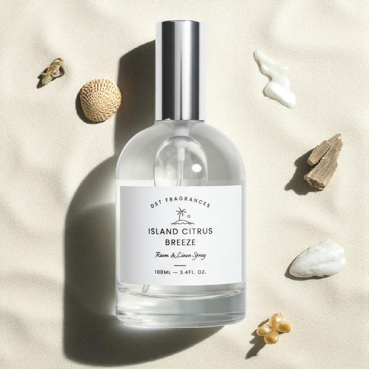 Bottle of 'Island Citrus Breeze' room & linen spray on a sandy background with seashells.