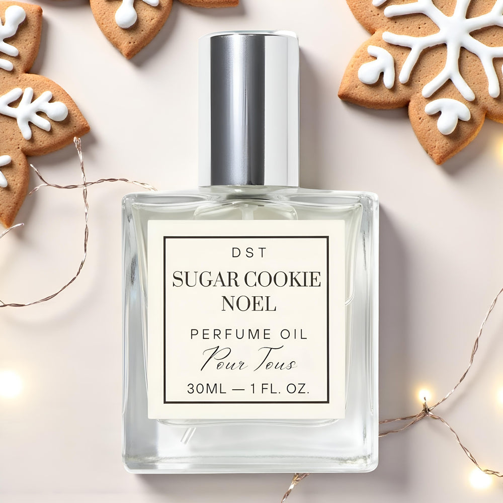 Perfume oil bottle labeled 'Sugar Cookie Noel' with gingerbread cookies and fairy lights in the background