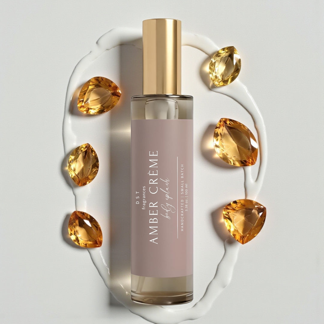 100ml bottle of Amber Crème scented Body Splash by DST Fragrances against a white background with amber gemstones and spilled cream.