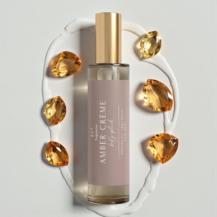 100ml bottle of Amber Crème scented Body Splash by DST Fragrances against a white background with amber gemstones and spilled cream.