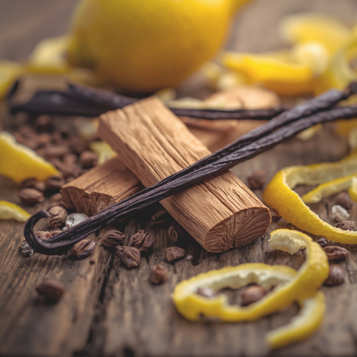 Vanilla wood sticks and vanilla beans arranged on a rustic wooden surface with lemon zest, vanilla seeds, and a blurred lemon in the background.