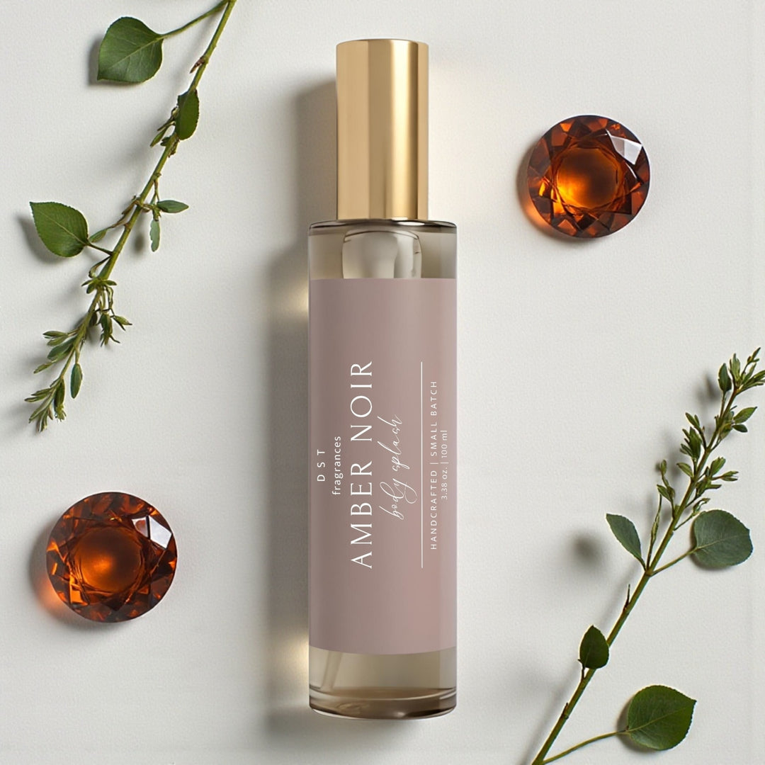 100ml bottle of Amber Noir scented Body Splash by DST Fragrances against a white background with Amber gemstones and greenery.