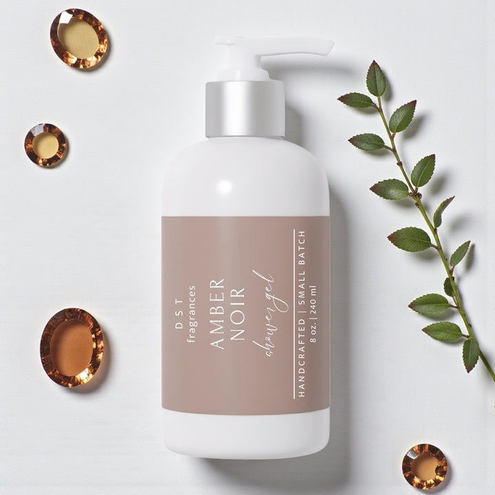 240ml bottle of Amber Noir scented Shower Gel by DST Fragrances against a white background with Amber gemstones and greenery.