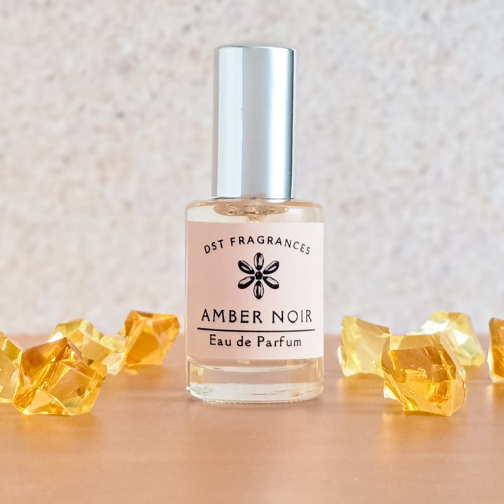 Amber Noir eau de parfum bottle with decorative yellow stones on a neutral background
