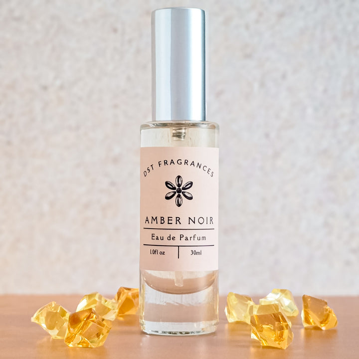 Perfume bottle labeled 'Amber Noir' by Dst Fragrances on a neutral background with yellow decorative elements.