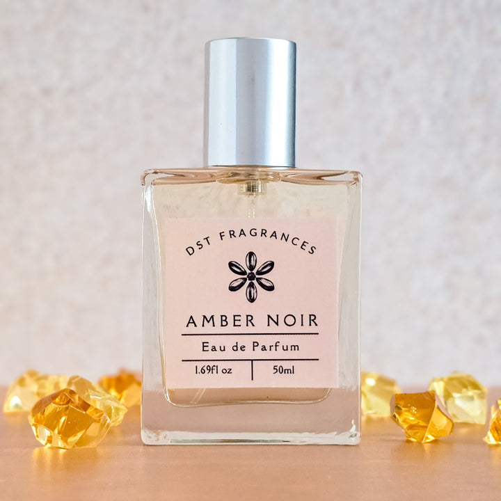 Perfume bottle labeled 'Amber Noir' by DST Fragrances on a light background with decorative elements.