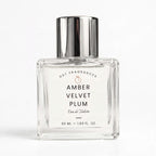 A 50 ml clear glass perfume bottle with a reflective silver cap, labeled 'AMBER VELVET PLUM' by DST FRAGRANCES, on a clean white background.