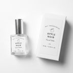 A clear glass perfume bottle with a silver cap next to its white rectangular box, both labeled 'DST FRAGRANCES APPLE NOIR Eau de Toilette 10 ML - 0.33 FL.