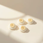Four small white whipped cream or frosting dollops, each topped with a thin sliced banana, arranged on a warm cream surface with soft diagonal sunlight and shadows.