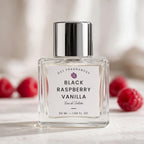 A 50 ml bottle of DST Fragrances Black Raspberry Vanilla Eau de Toilette, featuring a clear glass bottle, white label, and a shiny silver cap, set against a soft-focus background with fresh raspberries.