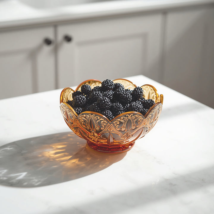 An amber glass bowl filled with blackberries sits on a white marble countertop in a bright kitchen setting.