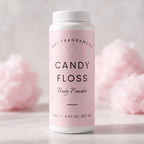 A white plastic bottle of DST Fragrances Candy Floss Body Powder with a light pink label, set against a soft-focus background of pink cotton candy on a light marble surface.