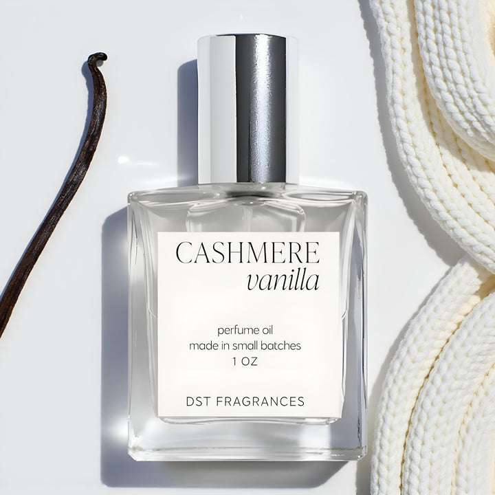 30ml bottle Cashmere Vanilla Perfume Oil by DST Fragrances on a ivory backdrop with vanilla bean and cashmere scarf in the background.