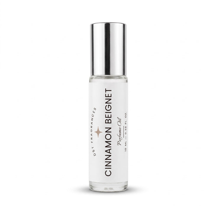 A 10 ml glass rollerball bottle of Cinnamon Beignet perfume oil by 051 Fragrances, featuring a clear glass body, white label, and a reflective silver metallic cap, set against a plain white background.