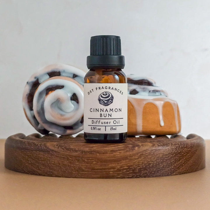 Bottle of Cinnamon Bun diffuser oil on a wooden coaster with cinnamon bun decorations in the background.