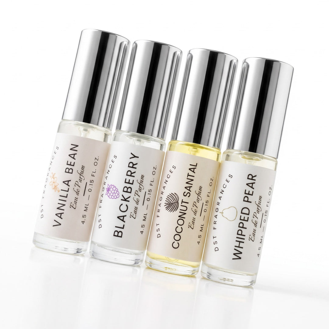 Four small clear glass perfume bottles with silver caps and white labels, arranged in a row on a white background. The labels read Vanilla Bean, Blackberry, Coconut Santal, and Whipped Pear, with Dst Fragrances branding visible.