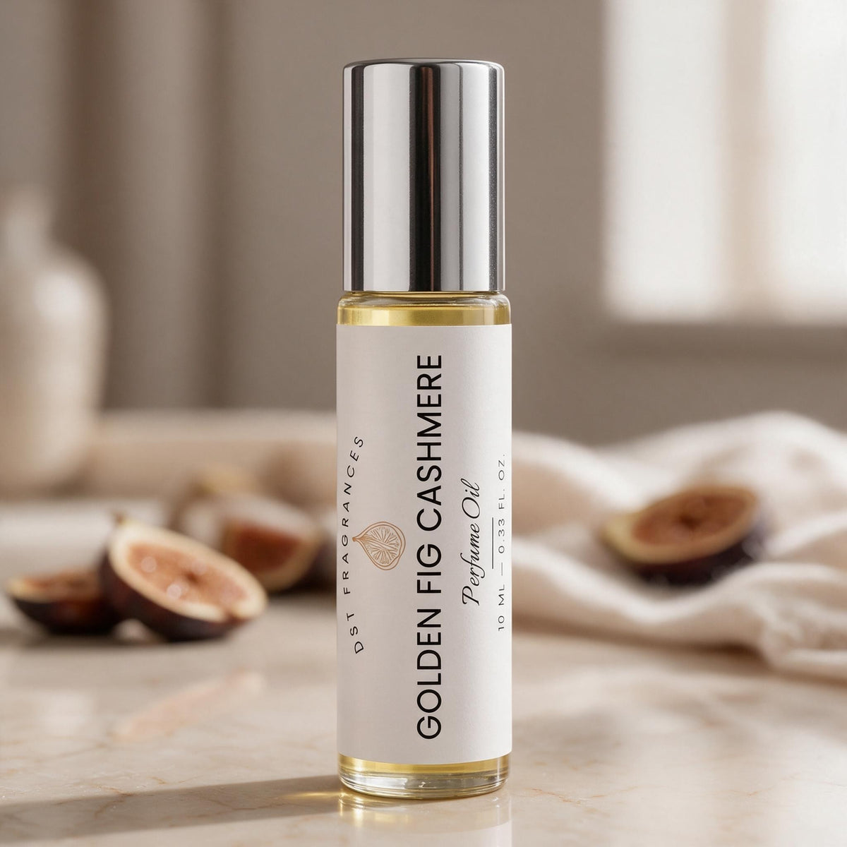 A clear glass bottle of Golden Fig Cashmere perfume oil with a shiny silver cap and a white label, standing on a marble surface with figs and a soft neutral background.