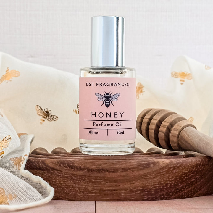 Perfume oil bottle labeled 'Honey' by DST Fragrances on a wooden tray with a honeycomb and bees.
