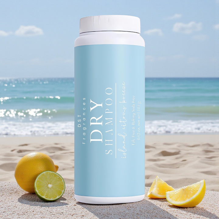 114g bottle of Island Citrus Breeze scented Dry Shampoo Powder by DST Fragrances sitting on a sandy beach with Lemons and Limes and the ocean in the background.