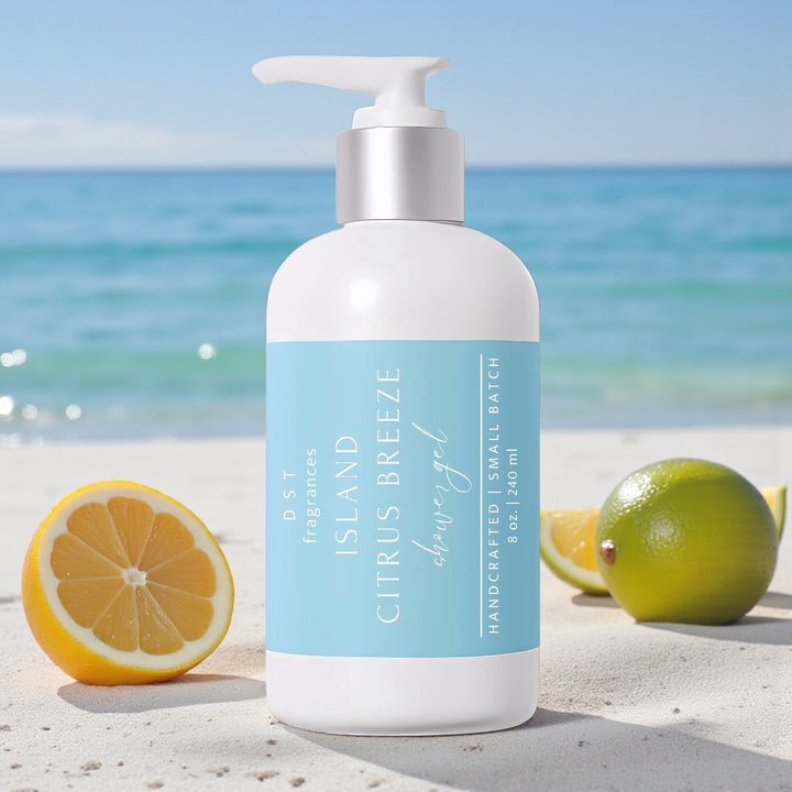 240ml bottle of Island Citrus Breeze scented Shower gel by DST Fragrances sitting on a sandy beach with Lemons and Limes and the ocean in the background.