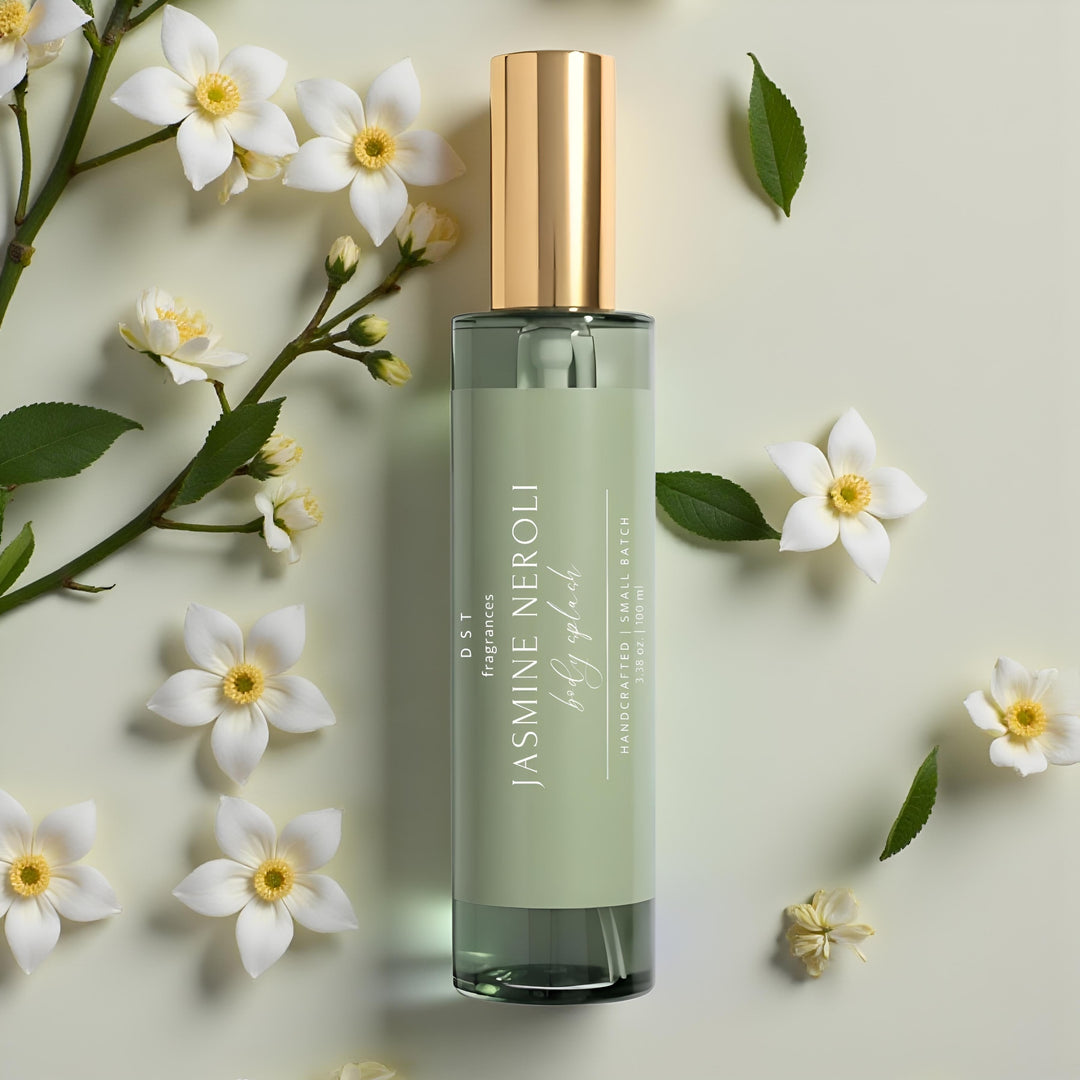 100ml bottle of Jasmine Neroli body splash by DST Fragrances laying on a light green surface with jasmine flowers and green leaves in the background.