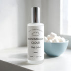 A bottle of DST Fragrances Marshmallow Cloud Body Splash, set on a light gray surface with a light blue bowl of marshmallows in the background.