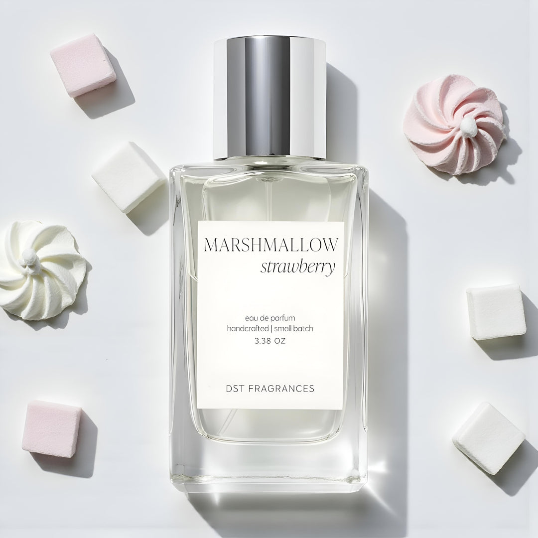 100ml bottle of Marshmallow Strawberry Eau de Parfum by DST Fragrances laying on an ivory surface with pink and white marshmallows and a dollop of white whipped cream in the background.