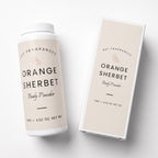 A white plastic bottle and matching rectangular box for DST Fragrances Orange Sherbet Body Powder, shown on a clean white background. The packaging features a warm beige label with black text and a small orange slice illustration.