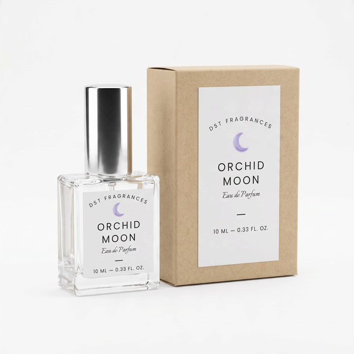 A 10 mL clear glass perfume bottle with a silver cap stands next to its kraft paper box. Both the bottle and box feature a white label with the brand name &