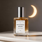 A 30 ml bottle of DST Fragrances Patchouli Moon Eau de Parfum with amber liquid and a silver cap, set on a white surface against a dark gray background with a warm crescent moon light.
