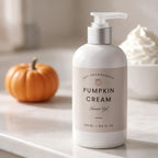 A bottle of DST Fragrances Pumpkin Cream Shower Gel stands on a light marble countertop. The bottle is white with a silver pump and a beige label.