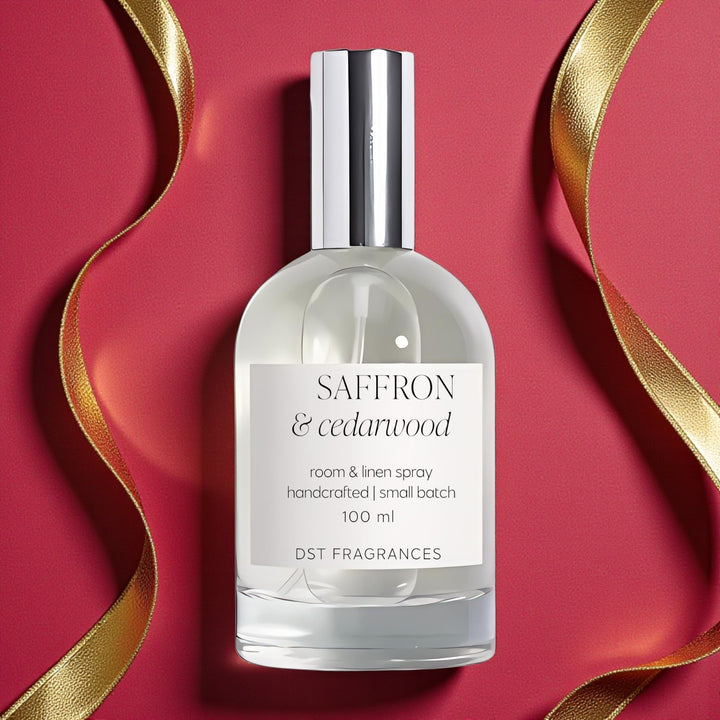 100ml bottle of Saffron Cedarwood Room Linen by DST Fragrances against a red background with gold bokeh lights.