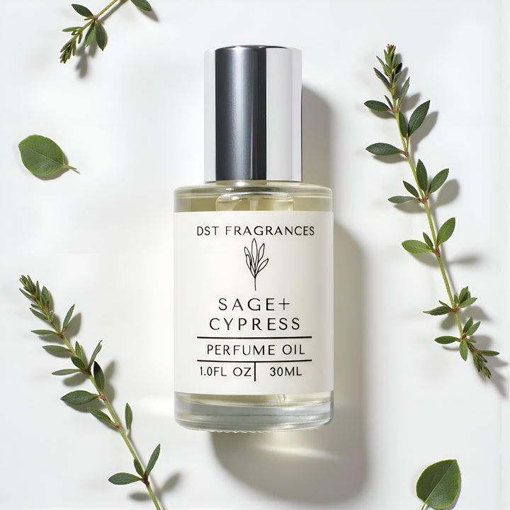 Bottle of Sage + Cypress perfume oil with green leaves on a white background