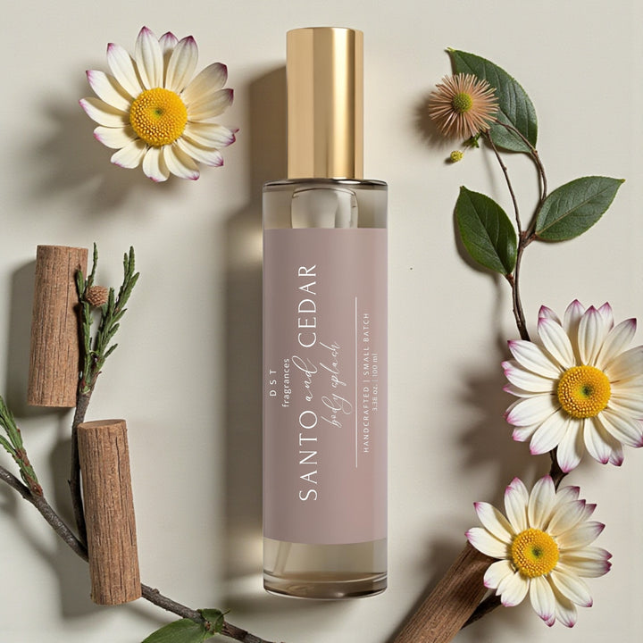 100ml bottle of Santo & Cedar scented Body Splash by DST Fragrances lying flat on a beige background surrounded by pink and white daisy flowers.
