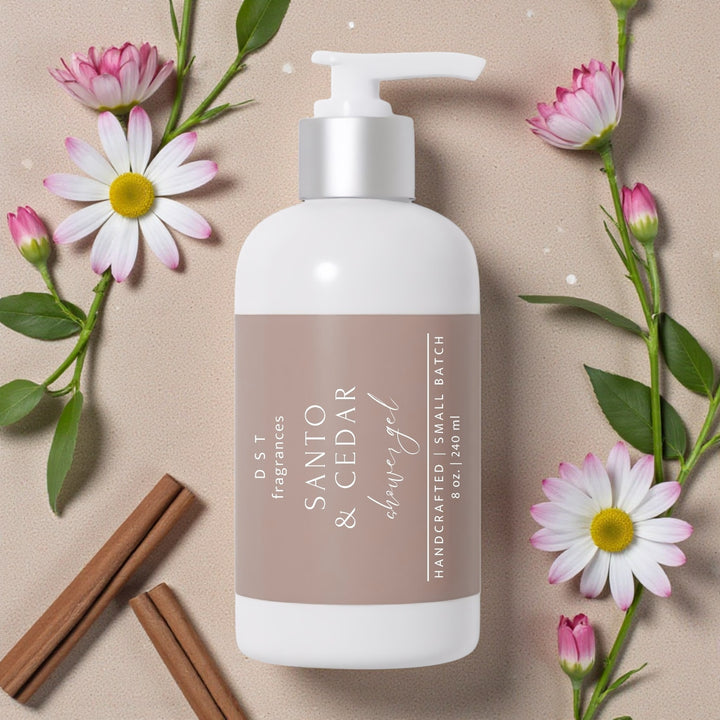 240ml bottle of Santo & Cedar scented Shower Gel by DST Fragrances lying flat on a beige background surrounded by white and pink Daisy flowers.