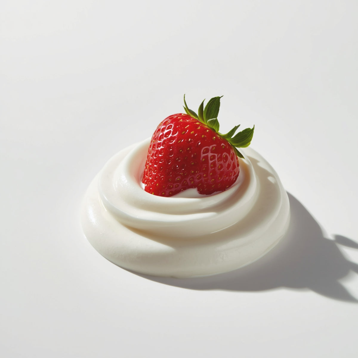 A single strawberry with green leaves sits centered on a swirl of white whipped cream or yogurt against a clean white background.