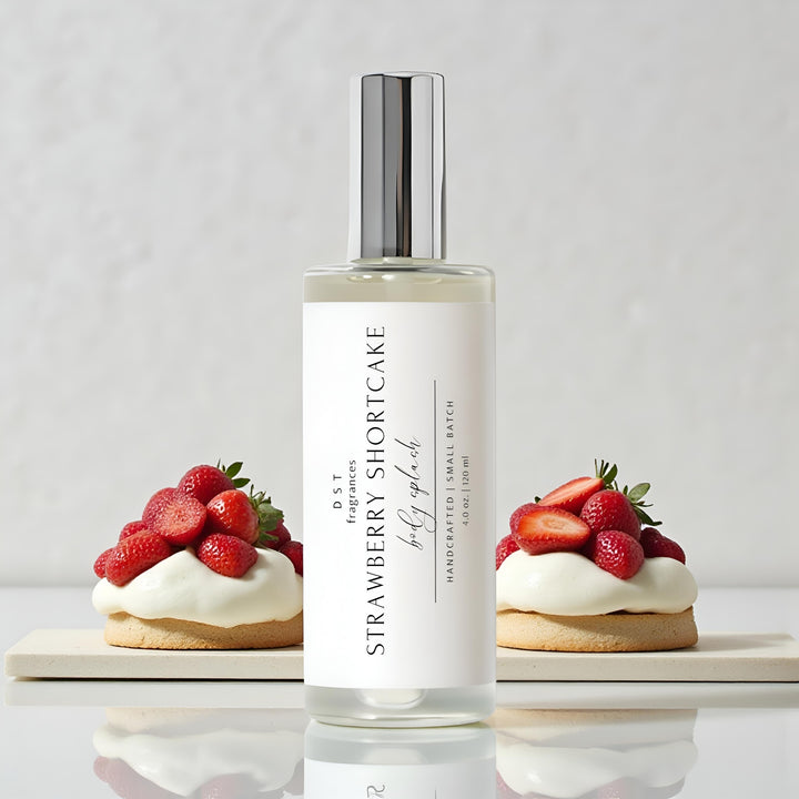 4oz bottle of Strawberry Shortcake body splash by DST Fragrances sitting on a glossy white surface with 2 strawberry shortcake desserts against a light grey background.