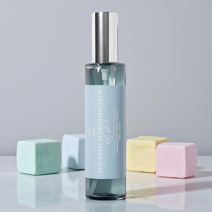 100ml bottle of Sugared marshmallow body splash by dst fragrances sitting on a white glossy surface with pastel colored marshmallows against a light grey backdrop.