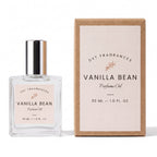 A bottle of DST Fragrances Vanilla Bean Perfume Oil next to its brown kraft paper packaging box, both featuring a pale pink label with black text.