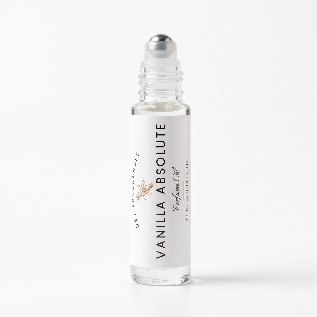 A 10 mL clear glass rollerball bottle of Vanilla Absolute perfume oil by DST Fragrances, featuring a white label with black text and a small gold starburst logo, topped with a silver cap, set against a clean white background.