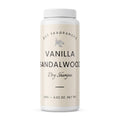 A white plastic bottle of DST Fragrances Vanilla Sandalwood Dry Shampoo, featuring a cream-colored label with black text and a small botanical illustration, set against a plain white background.