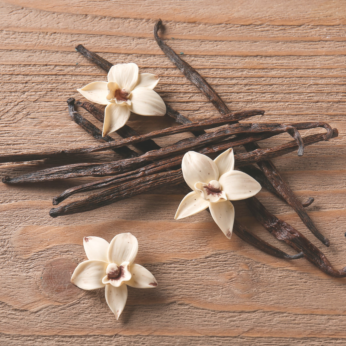 Vanilla beans and vanilla flowers arranged on a rustic wooden surface.