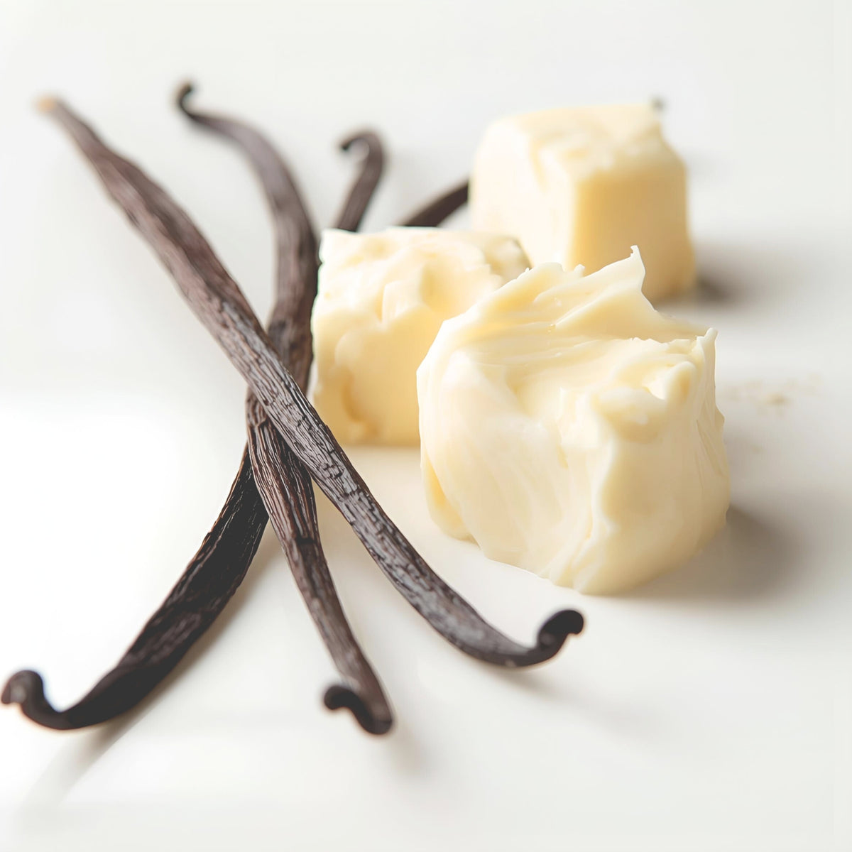 Vanilla beans and chunks of creamy butter arranged on a clean white surface.