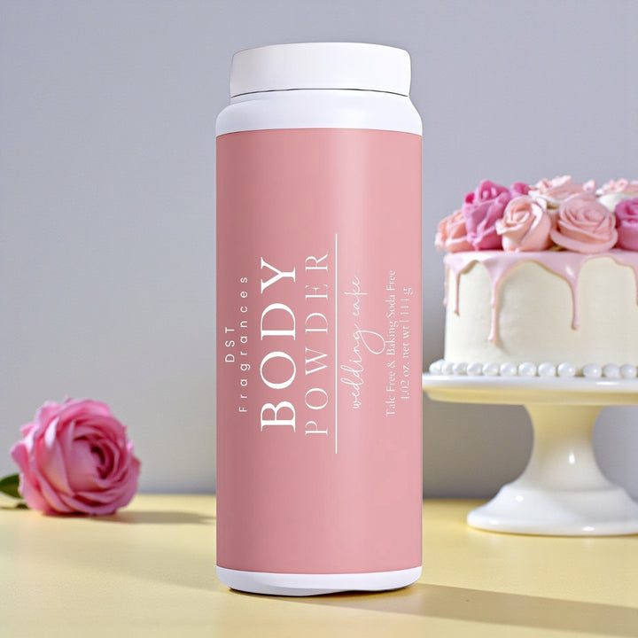 114g bottle of Wedding Cake scented body powder by DST Fragrances sitting on a pale-yellow surface with light grey background and a white wedding cake with Pink Roses.