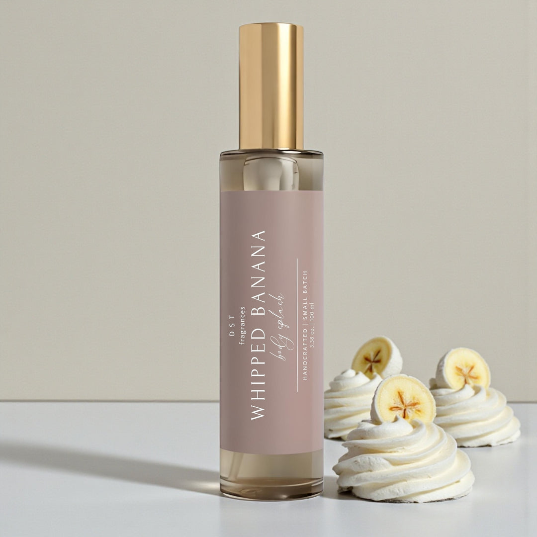 100ml bottle of Whipped Banana scented body splash by DST Fragrances sitting on a white surface with dollops of whipped cream and sliced bananas against a tan background.