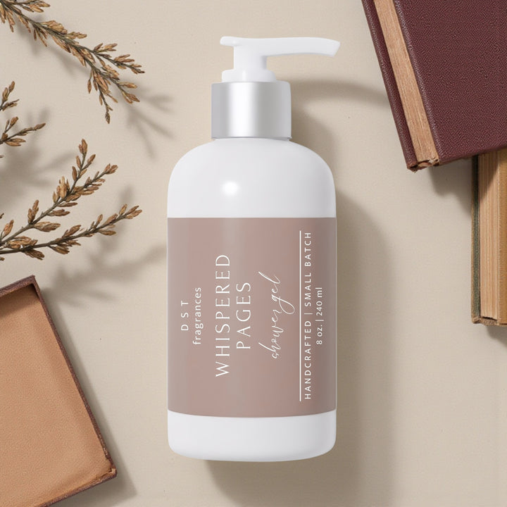240ml bottle of Whispered Pages scented shower gel by DST Fragrances against an ivory background with 3 brown leather-bound books and greenery.